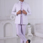 Man dressed in a lavender Jodhpuri suit with a diamond pattern, featuring a high collar and buttoned front, set in a minimalist interior with white walls.