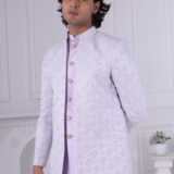 Man dressed in a lavender Jodhpuri suit with a diamond pattern, featuring a high collar and buttoned front, set in a minimalist interior with white walls.
