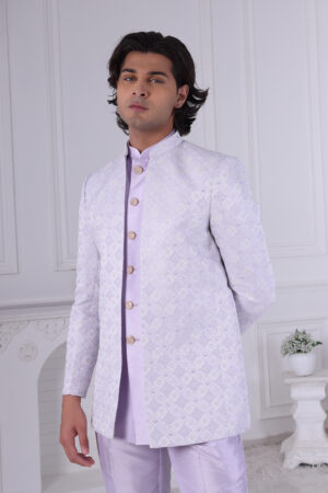 Man dressed in a lavender Jodhpuri suit with a diamond pattern, featuring a high collar and buttoned front, set in a minimalist interior with white walls.
