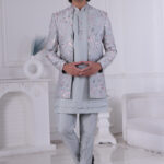 Man wearing a pastel blue floral embroidered Jodhpuri suit with matching kurta and trousers, posing indoors with hands clasped.