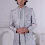 Man wearing a pastel blue floral embroidered Jodhpuri suit with matching kurta and trousers, posing indoors with hands clasped.