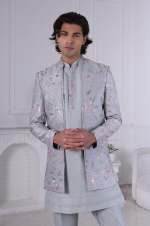 Man wearing a pastel blue floral embroidered Jodhpuri suit with matching kurta and trousers, posing indoors with hands clasped.
