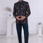 Man wearing a navy blue printed Jodhpuri suit with floral patterns and metallic buttons, standing indoors.