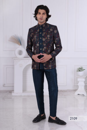 Man wearing a navy blue printed Jodhpuri suit with floral patterns and metallic buttons, standing indoors.