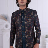 Man wearing a navy blue printed Jodhpuri suit with floral patterns and metallic buttons, standing indoors.