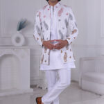 Man wearing a white Jodhpuri suit with multicolor leaf and butterfly prints, standing indoors with folded arms.