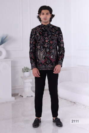 Man wearing a black embroidered Jodhpuri suit with multicolor floral and bird motifs, posing indoors with hands clasped.