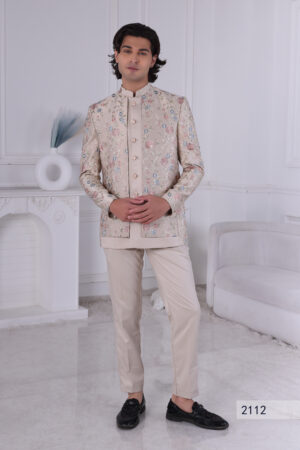 Man wearing a beige Jodhpuri suit with pastel floral embroidery and metallic buttons, posing indoors.