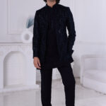 Man wearing a navy blue textured Jodhpuri suit with subtle embroidery and sequins, posing indoors with hands on jacket.