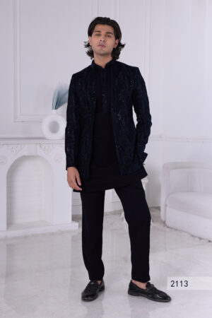 Man wearing a navy blue textured Jodhpuri suit with subtle embroidery and sequins, posing indoors with hands on jacket.