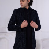 Man wearing a navy blue textured Jodhpuri suit with subtle embroidery and sequins, posing indoors with hands on jacket.