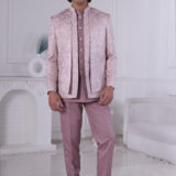 Man wearing a lavender textured Jodhpuri suit with subtle embroidery and metallic buttons, standing indoors with hands clasped.