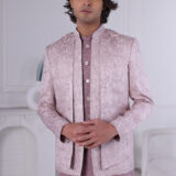 Man wearing a lavender textured Jodhpuri suit with subtle embroidery and metallic buttons, standing indoors with hands clasped.