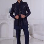 Man wearing a navy blue Jodhpuri suit with embroidered vertical stripes and mirror accents, standing indoors.