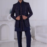 Man wearing a navy blue Jodhpuri suit with embroidered vertical stripes and mirror accents, standing indoors.