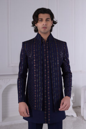 Man wearing a navy blue Jodhpuri suit with embroidered vertical stripes and mirror accents, standing indoors.