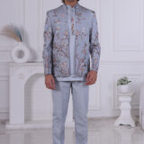 Man wearing a sky blue embroidered Jodhpuri suit with floral and nature-inspired motifs, posing indoors.