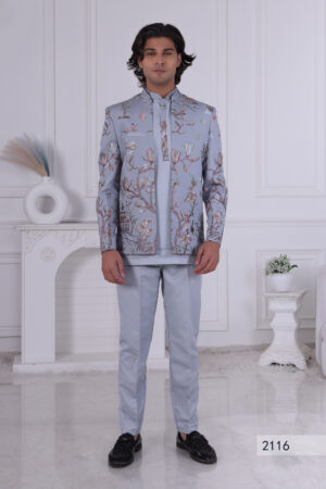 Man wearing a sky blue embroidered Jodhpuri suit with floral and nature-inspired motifs, posing indoors.
