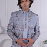 Man wearing a sky blue embroidered Jodhpuri suit with floral and nature-inspired motifs, posing indoors.