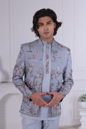 Man wearing a sky blue embroidered Jodhpuri suit with floral and nature-inspired motifs, posing indoors.