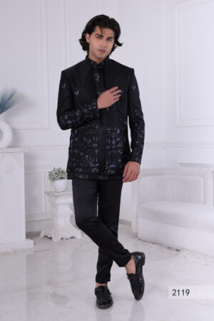 Man wearing a black embroidered Jodhpuri suit with multicolor floral patterns and studded detailing, posing indoors.