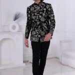 Man wearing a black velvet embroidered Jodhpuri suit with metallic floral patterns, posing indoors.