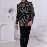 Man wearing a black velvet embroidered Jodhpuri suit with metallic floral patterns, posing indoors.