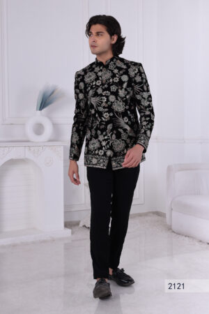Man wearing a black velvet embroidered Jodhpuri suit with metallic floral patterns, posing indoors.