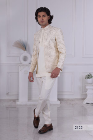 Man wearing a cream Jodhpuri suit with textured patterns, posing indoors with hands clasped.