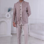 Man wearing a pastel pink textured Jodhpuri suit with metallic buttons, standing with hands clasped.