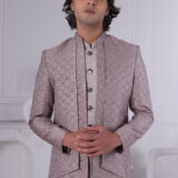 Man wearing a pastel pink textured Jodhpuri suit with metallic buttons, standing with hands clasped.