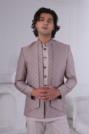 Man wearing a pastel pink textured Jodhpuri suit with metallic buttons, standing with hands clasped.
