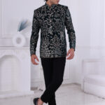 Man wearing a dark green velvet Jodhpuri suit with intricate floral, peacock, and dome embroidery.