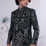 Man wearing a dark green velvet Jodhpuri suit with intricate floral, peacock, and dome embroidery.