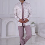 Man wearing a pastel lavender Jodhpuri suit with brocade deer and foliage motifs.