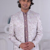 Man wearing a pastel lavender Jodhpuri suit with brocade deer and foliage motifs.