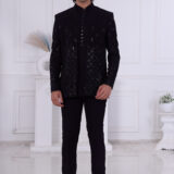 Man wearing a midnight black textured Jodhpuri suit with geometric patterns and metallic button detailing.