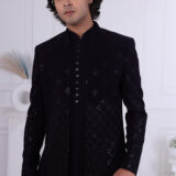 Man wearing a midnight black textured Jodhpuri suit with geometric patterns and metallic button detailing.