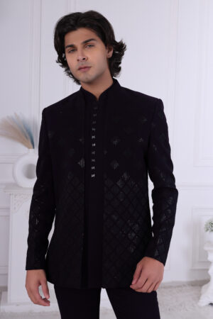 Man wearing a midnight black textured Jodhpuri suit with geometric patterns and metallic button detailing.