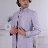 Man wearing a lavender silk brocade Jodhpuri suit with gold button detailing.