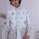 Man wearing an ice-blue Jodhpuri suit with detailed floral embroidery and silver buttons.