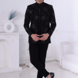 Man wearing a black Jodhpuri suit with floral embroidery, sequin highlights, and metallic triangular buttons.