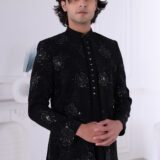 Man wearing a black Jodhpuri suit with floral embroidery, sequin highlights, and metallic triangular buttons.