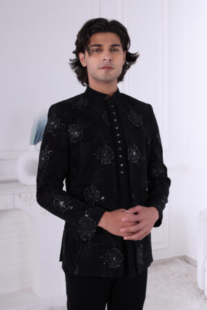 Man wearing a black Jodhpuri suit with floral embroidery, sequin highlights, and metallic triangular buttons.