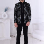 Man wearing a black velvet Jodhpuri suit with silver and blue crane embroidery and floral detailing.