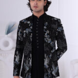 A man wearing a black velvet Jodhpuri suit with silver and blue crane embroidery and floral detailing.
