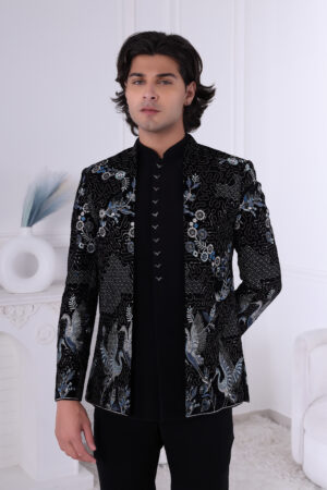 A man wearing a black velvet Jodhpuri suit with silver and blue crane embroidery and floral detailing.