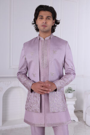 A man wearing a lavender Jodhpuri suit with metallic embroidery on the sleeves and hem, paired with a matching kurta and trousers.