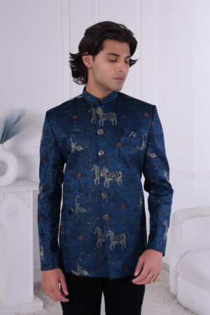 Man wearing a royal blue embroidered Jodhpuri suit with horse and crane motifs, styled with metallic buttons.