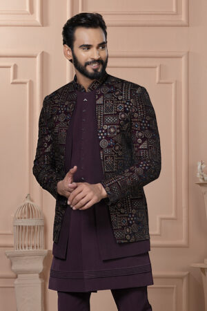 Man wearing a maroon Indo-Western outfit with an intricately embroidered mosaic-patterned jacket, standing against a peach-toned classic interior backdrop.